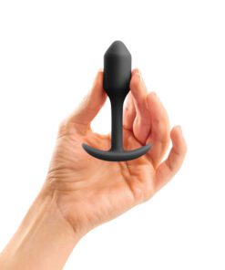 Hand holding a small sized, black Snug Plug butt plug covered withÂ  silicone on a white background